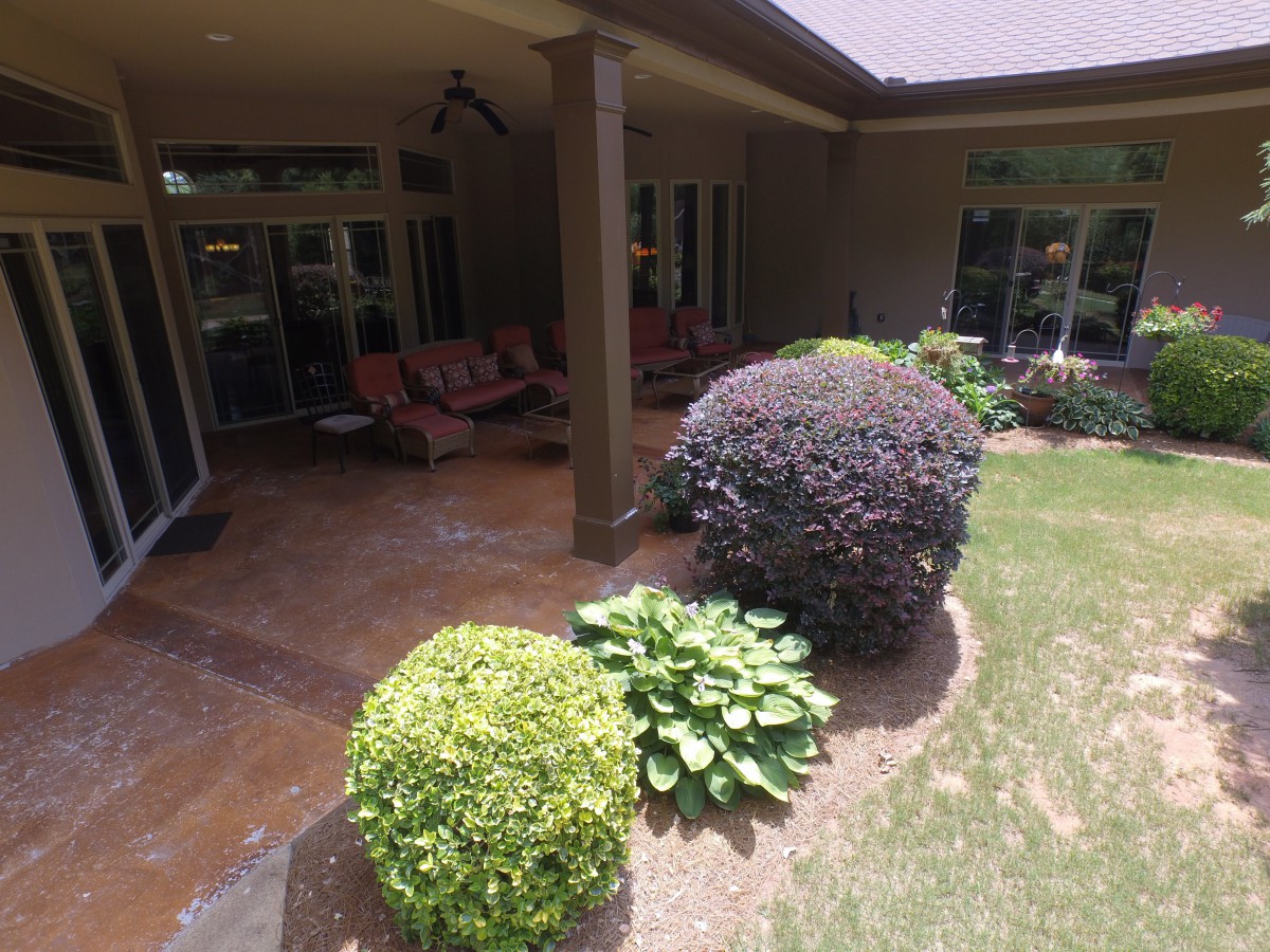 A cozy patio area with comfortable seating, surrounded by neatly trimmed shrubs and a well-maintained lawn.