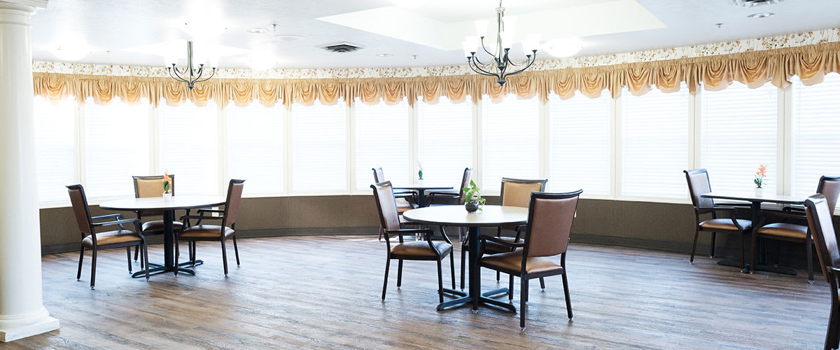A bright dining room with a table and chairs, illuminated by natural light streaming through large windows.
