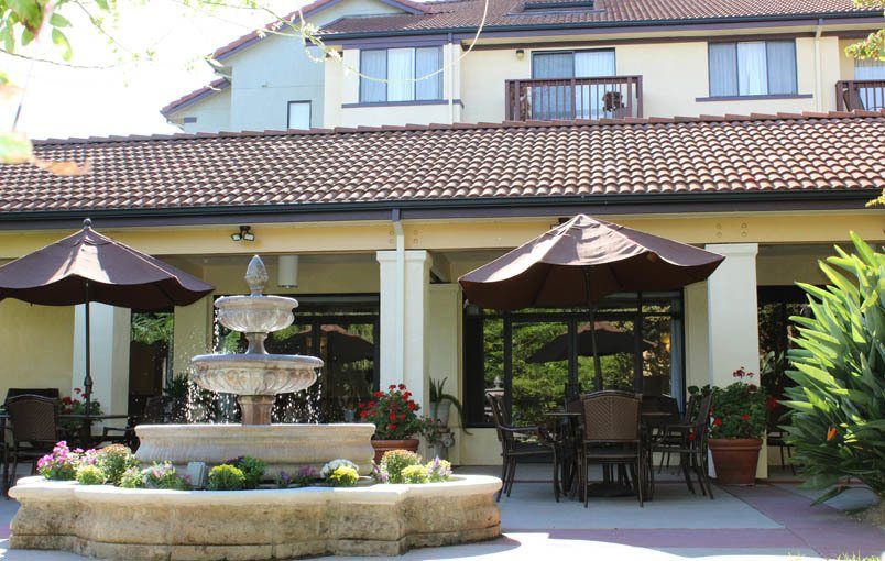 A tranquil outdoor patio area with a fountain and seating under large umbrellas.