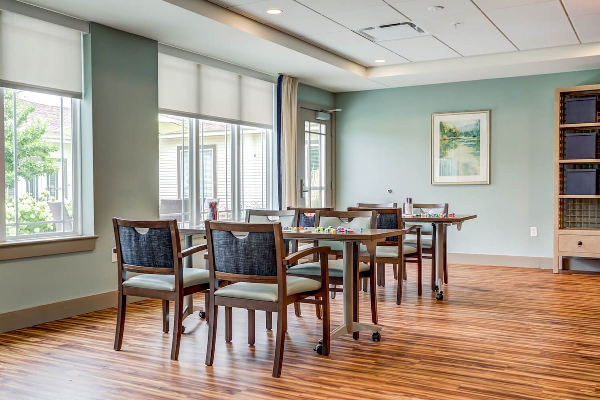 A modern dining room with several tables and chairs, featuring a wooden floor and large windows.