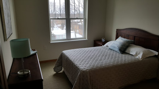 A cozy bedroom with a bed, nightstand, and large window letting in natural light.