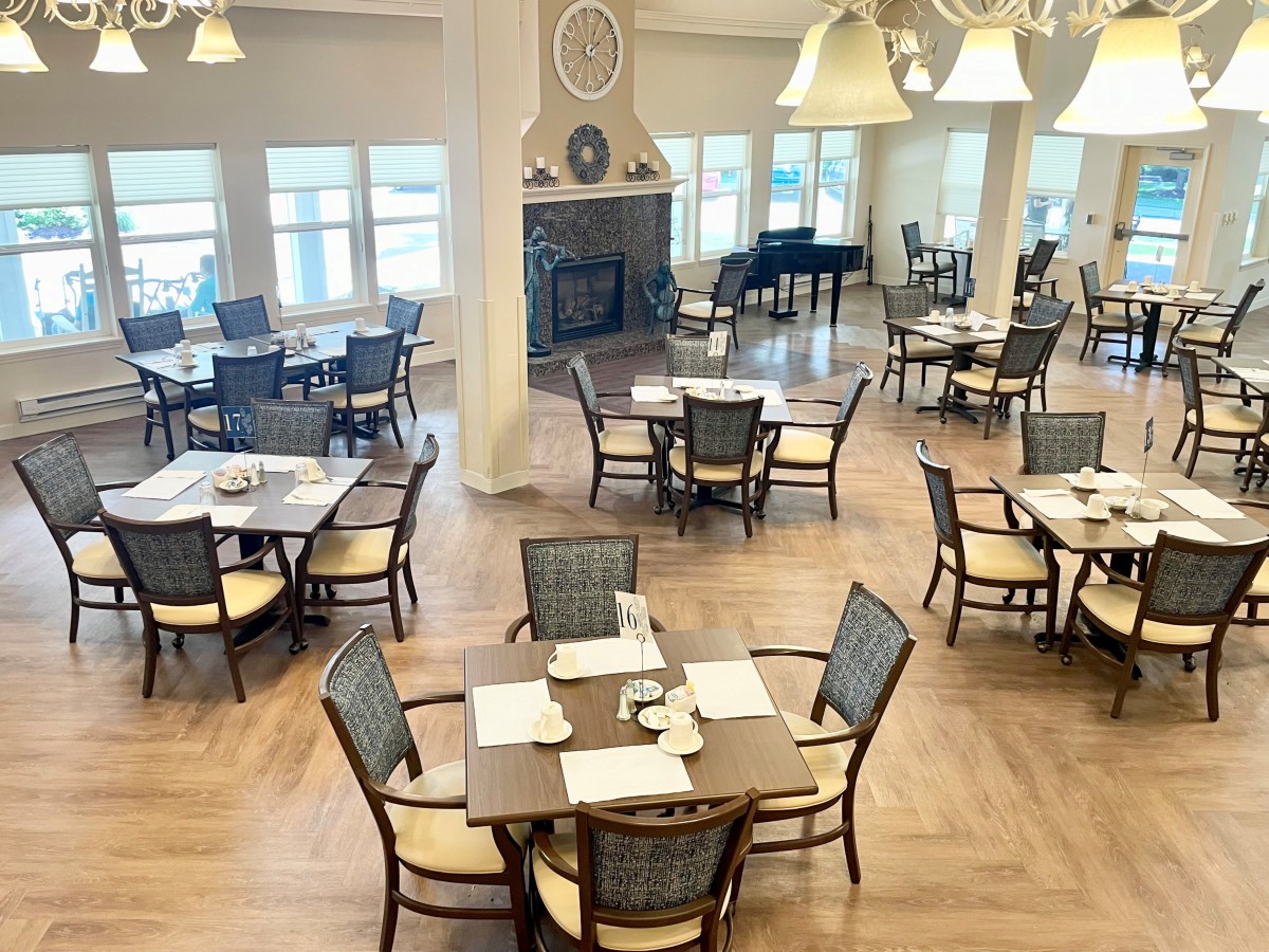 A spacious and elegantly designed dining area with neatly arranged tables and chairs, featuring warm lighting and a wooden floor.