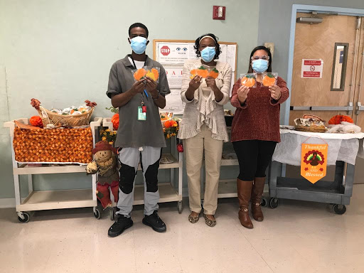 A group of three individuals celebrating Thanksgiving with festive decorations and holding up cards.