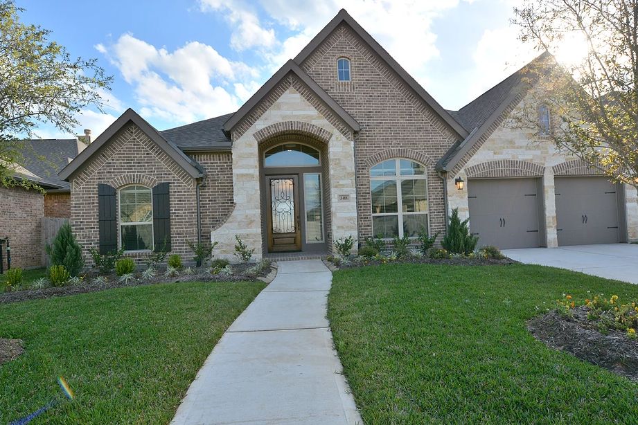 A brick house with a well-maintained front yard and driveway under a partly cloudy sky.