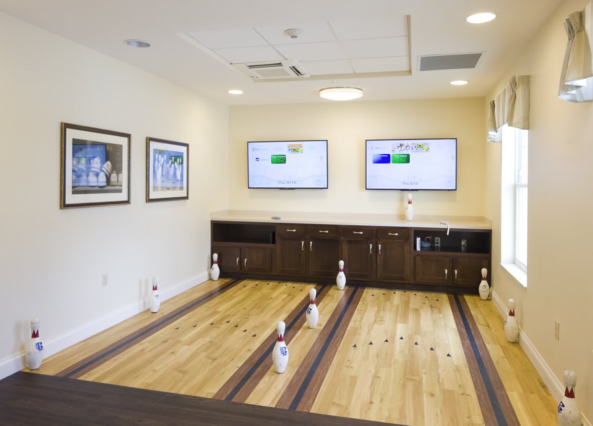 A stylish indoor mini bowling alley with wooden lanes and TV screens for entertainment.
