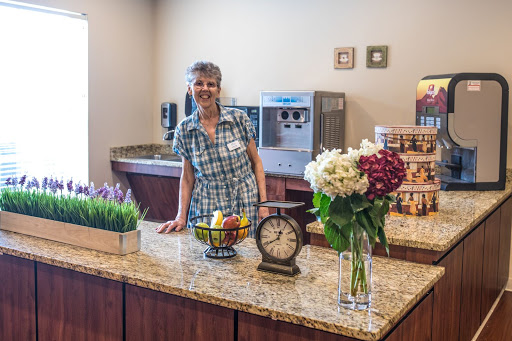 A friendly woman standing behind a beautifully arranged kitchen counter with flowers and fruit.