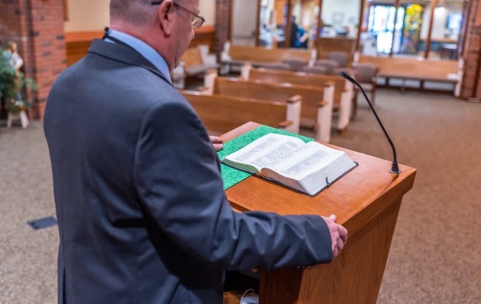A person at a lectern reading from the Bible in an empty church.