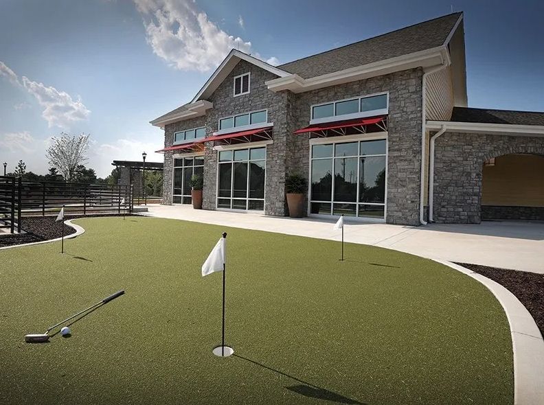 A modern building with a putting green in the foreground under a clear sky.