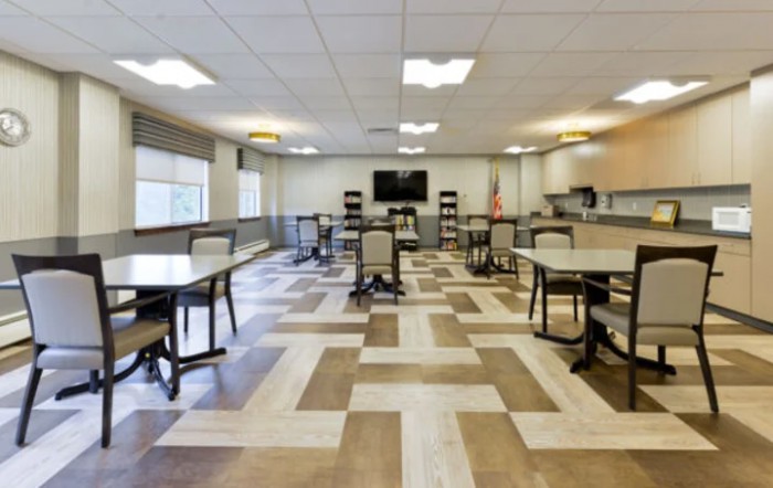 A modern dining area with tables and chairs arranged in an organized layout, featuring a neutral color scheme and ceiling lights.