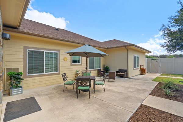 A landscaped patio with a table, chairs, and an umbrella outside a house.