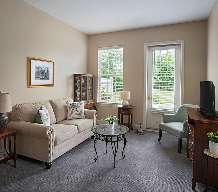 A cozy living room with a sofa, armchair, and a glass coffee table, decorated in neutral tones.
