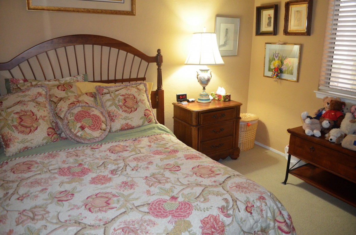 A cozy bedroom featuring a wooden bed with floral bedding, a lit bedside lamp, and framed artwork on the walls.