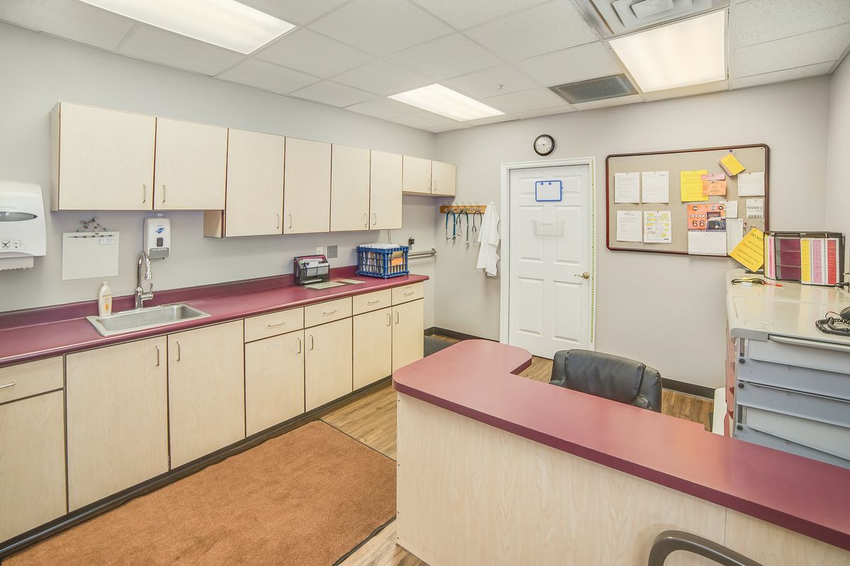 A clean and organized office with a desk, chairs, cabinets, and a bulletin board on the wall.