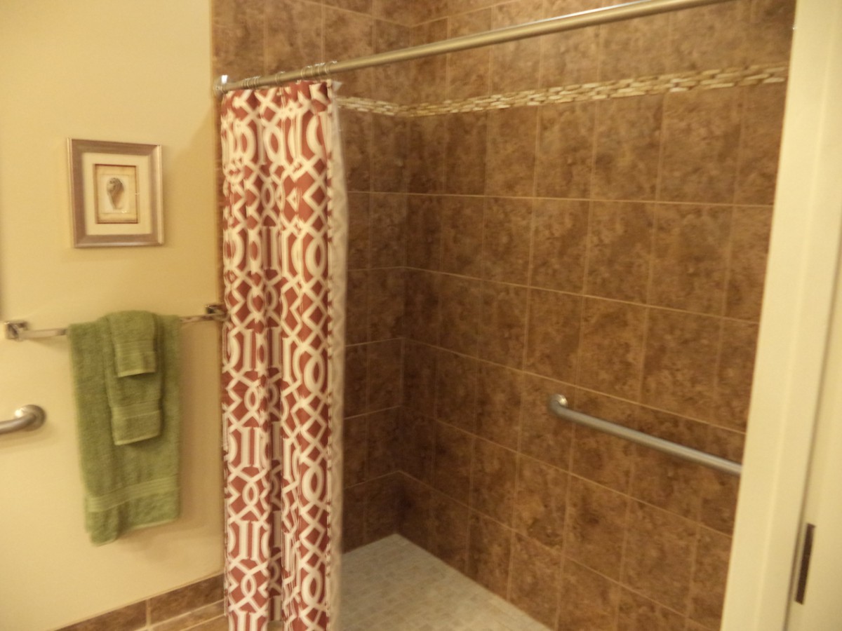 A cozy bathroom featuring a tiled shower with a patterned curtain and safety grab bar.