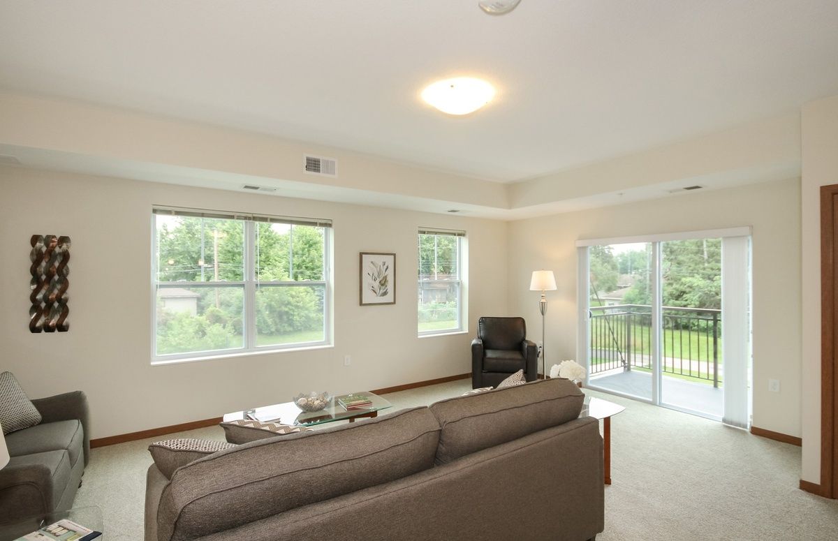 A modern living room with large windows and a balcony, featuring a comfortable sofa and an abundance of natural light.