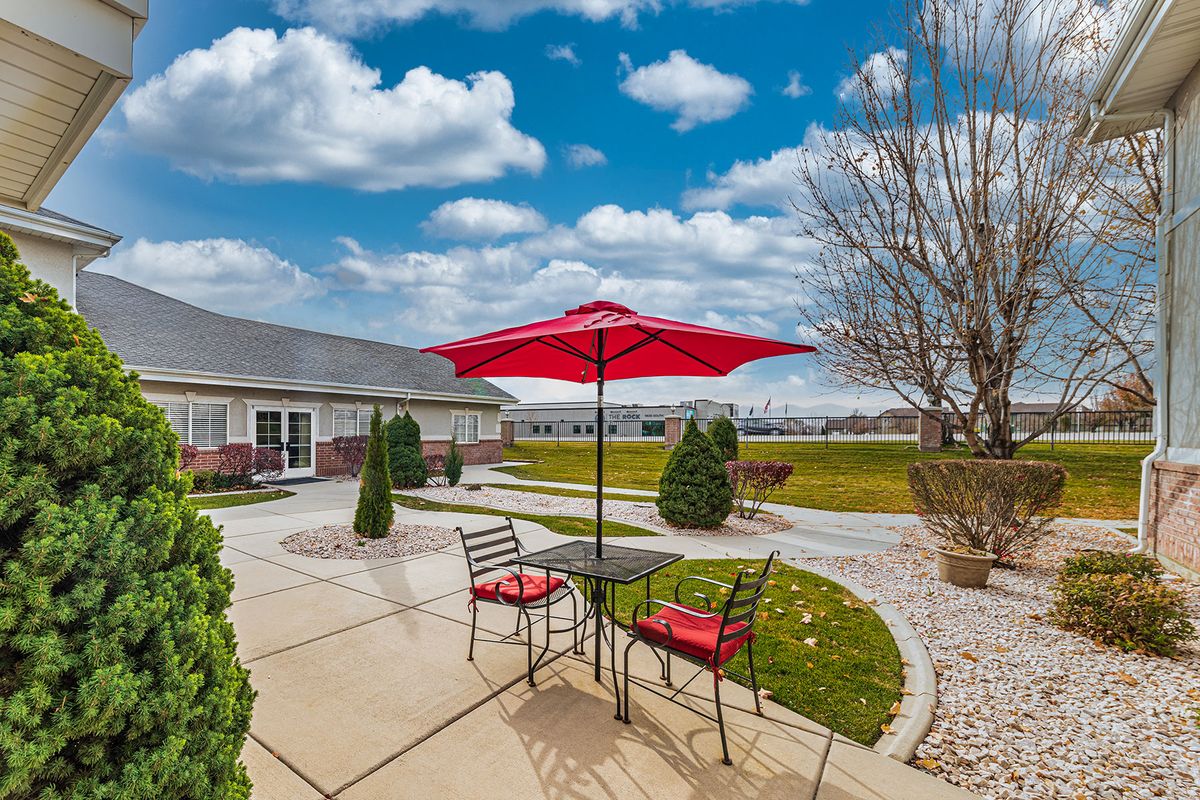 A cozy patio with a red umbrella and chairs under a bright, cloudy sky.