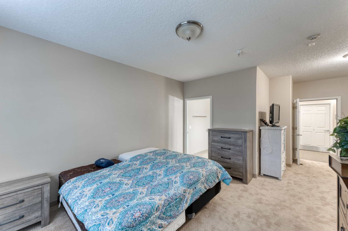 A spacious minimalist bedroom with a bed, dresser, and light fixture.