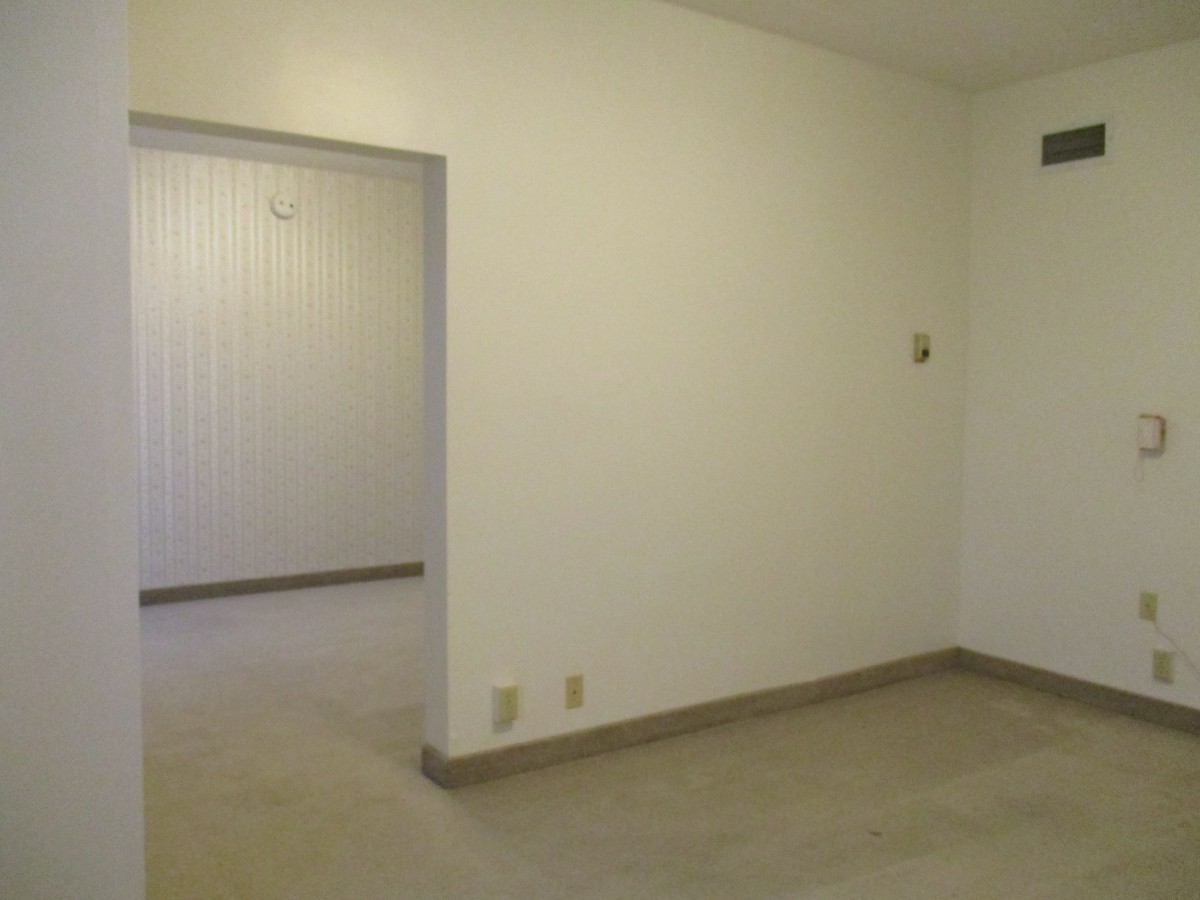 A minimalist empty room with white walls and carpet flooring.