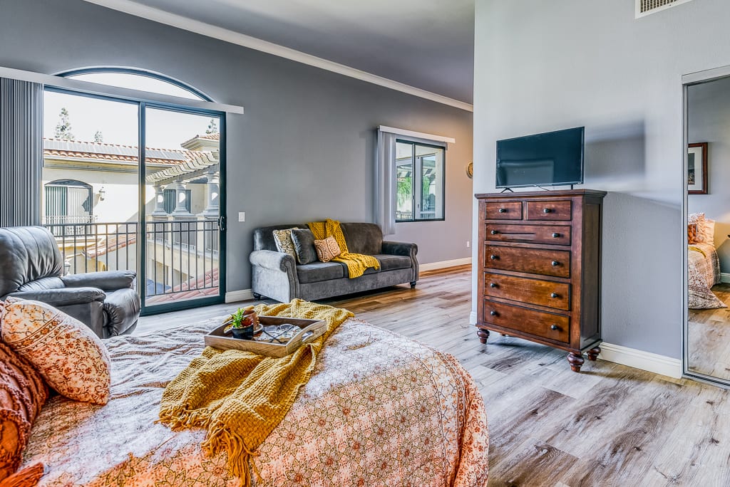 A cozy bedroom with modern decor, featuring a bed, sofa, dresser, and TV.