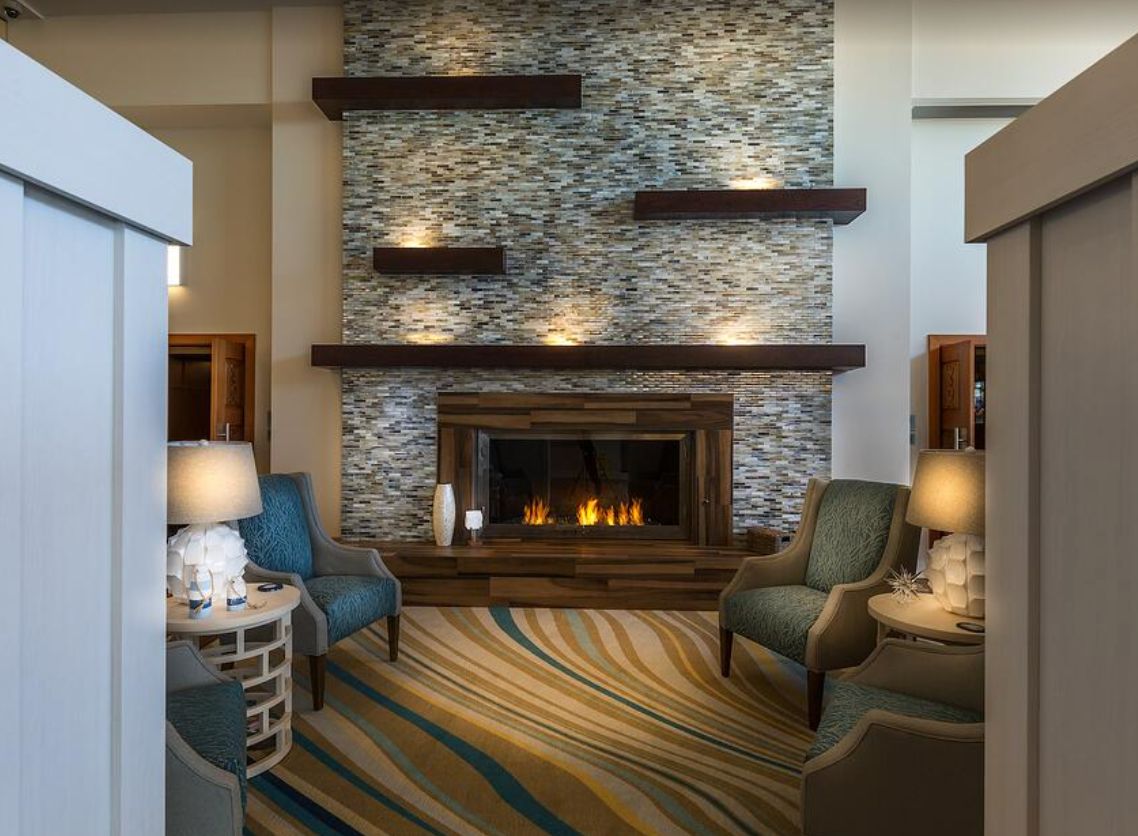 A modern living room with a stone fireplace, stylish shelving, and comfortable armchairs, creating a cozy atmosphere.