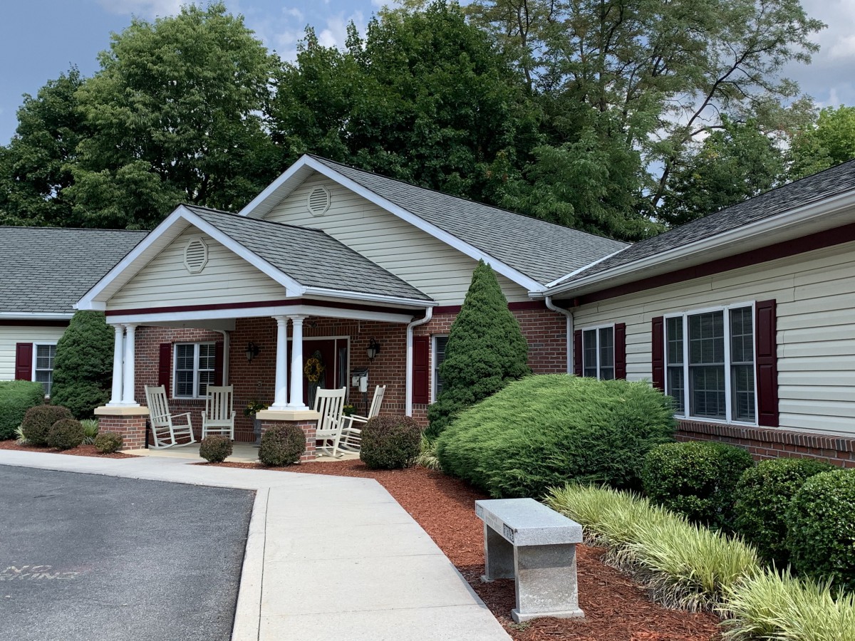 A suburban residential house with a porch, surrounded by trees and well-maintained landscaping.