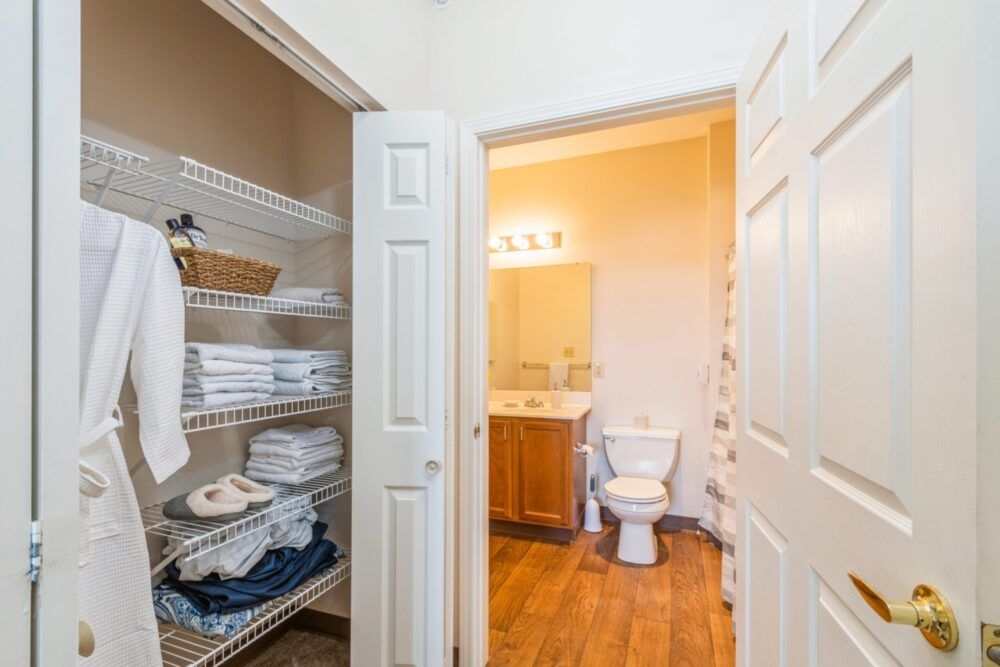 A bathroom with an adjacent linen closet, featuring a toilet and sink with a mirror above.