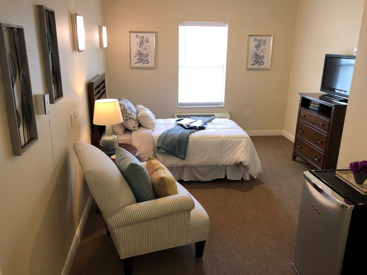 A cozy bedroom with a single bed, comfortable chair, and a lamp by the window.