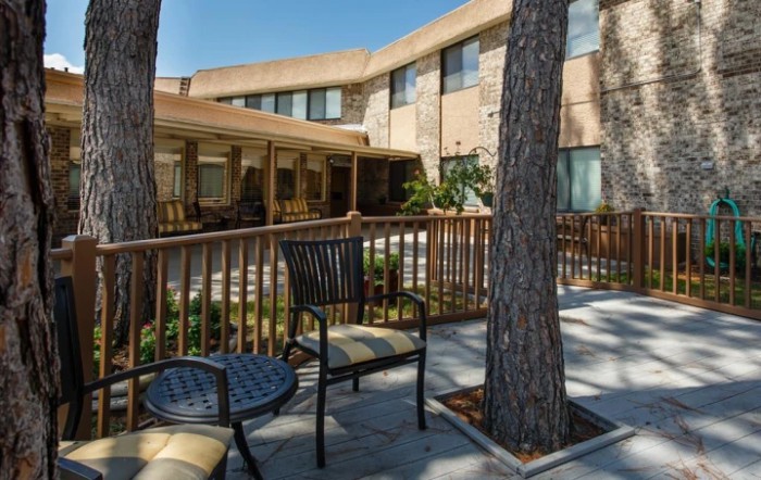A cozy outdoor patio area with chairs and tables, surrounded by trees and adjacent to a building.