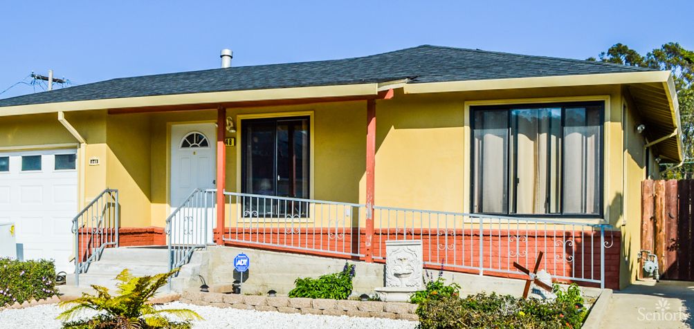 A yellow and orange house with a sloped roof and front yard.