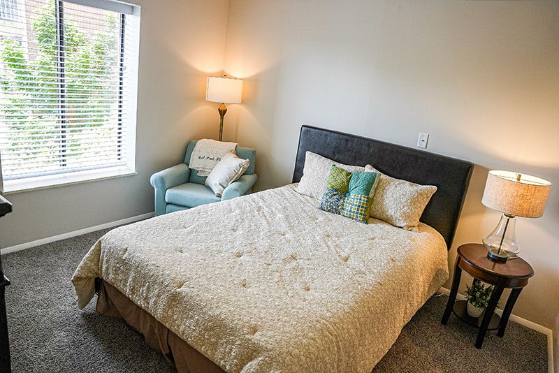 A cozy bedroom with a neatly made bed, accent chair, and warm lighting.