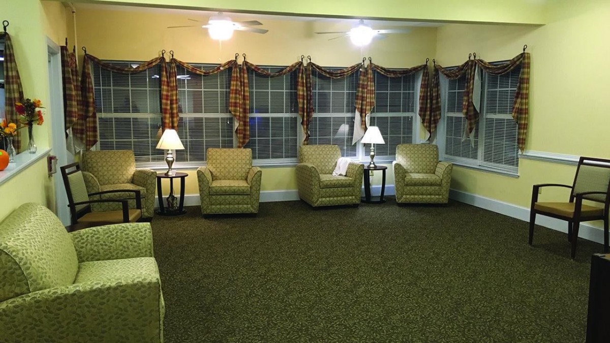 A cozy living room with several armchairs and lamps arranged by large windows.