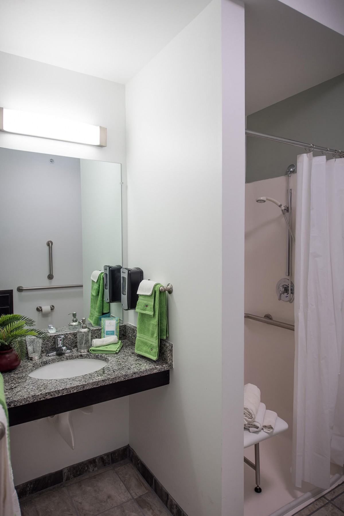 A clean and well-lit bathroom with a sink, mirror, towels, and a shower area.