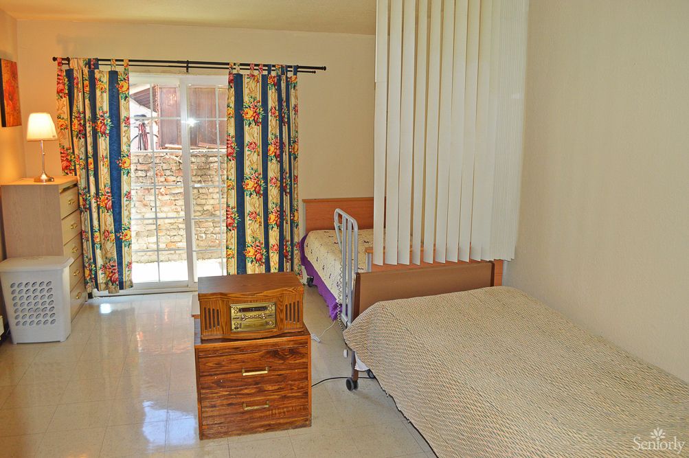 A bright room featuring a hospital bed, wooden furniture, and colorful curtains.