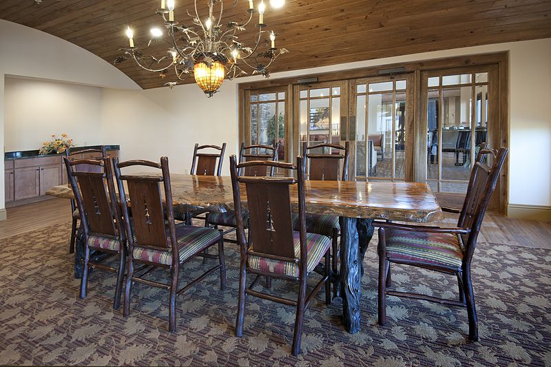 A rustic dining room with a large wooden table and chairs, illuminated by an elegant chandelier.