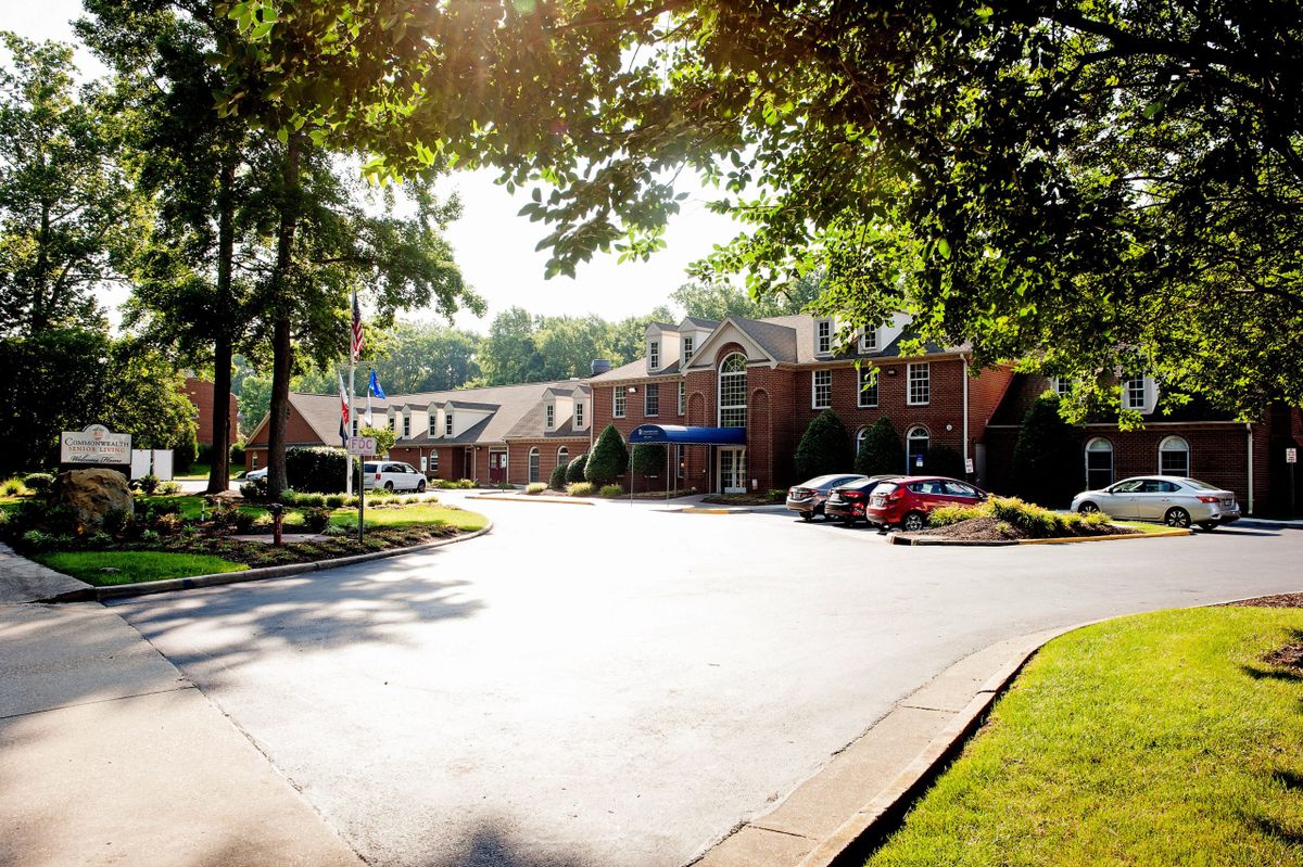 A sunlit brick building with a parking area surrounded by trees.