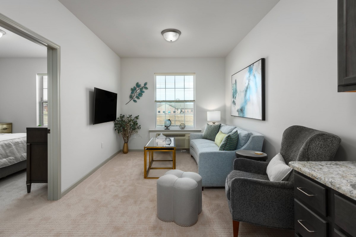 A cozy living room with modern furnishings, featuring a sofa, armchairs, and a large window.