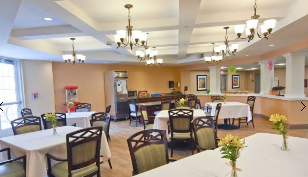 A well-lit dining area with multiple tables and chairs, adorned with chandeliers and a popcorn machine in the corner.