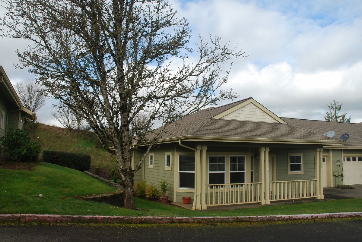 A suburban house with a large tree and well-maintained lawn under a partly cloudy sky.