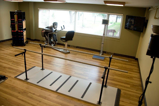 A view of a rehabilitation gym featuring exercise equipment, including a stationary bicycle and a barre for support.