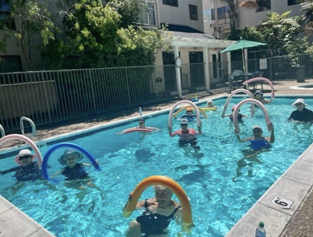 A group of people participating in an aquatic aerobics class using pool noodles.