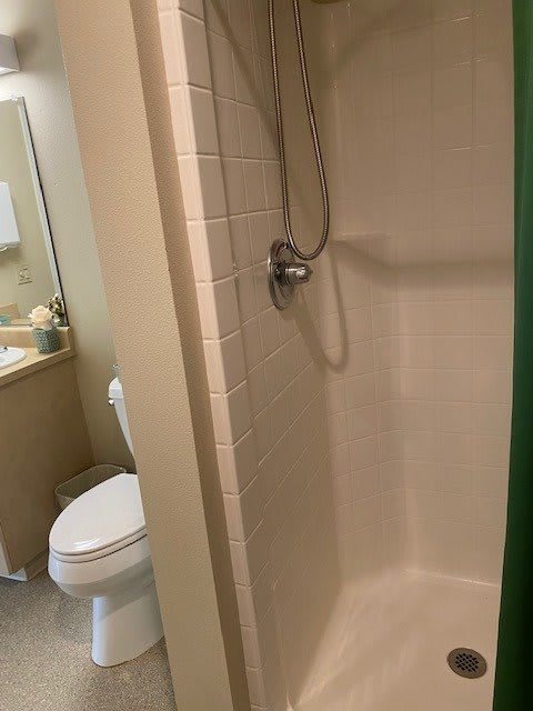 A small bathroom featuring a shower, toilet, and sink with a mirror.