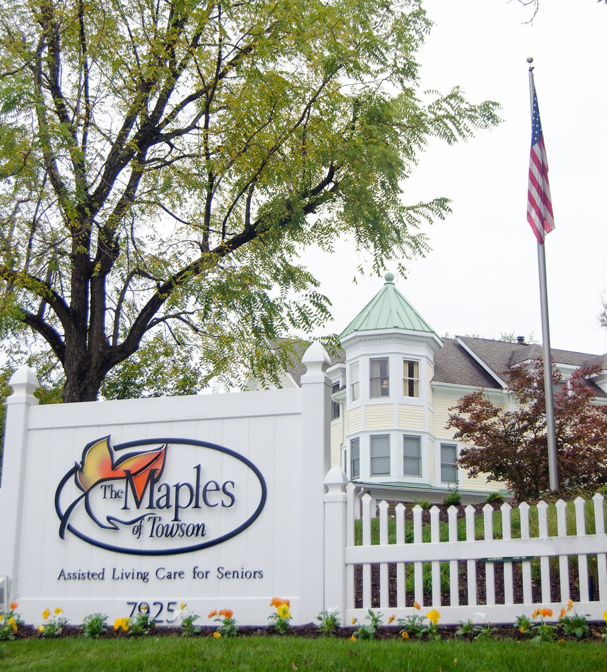Sign for The Maples Retirement Community with building and American flag in the background.