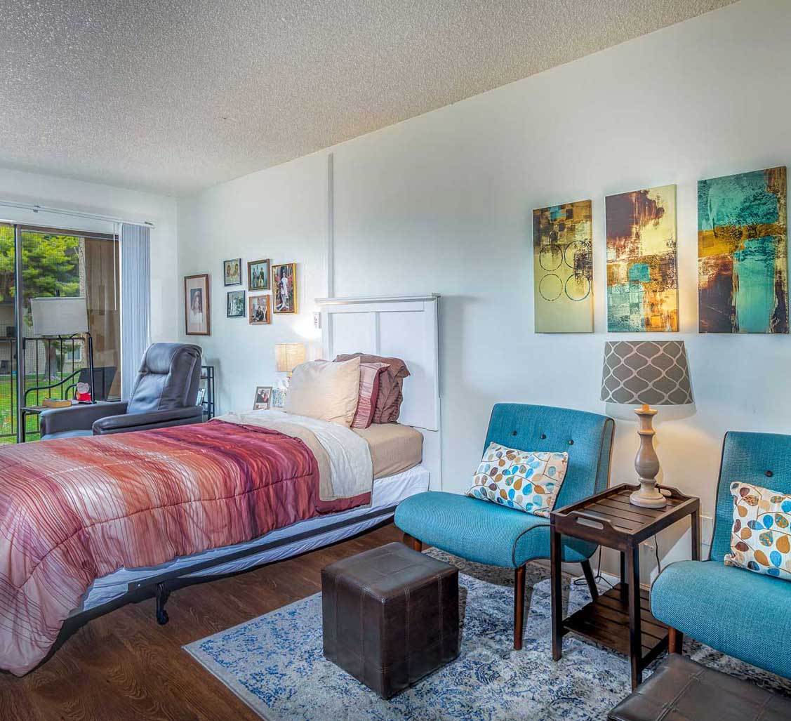 A cozy and modern bedroom featuring colorful bedding, artwork, and comfortable seating.