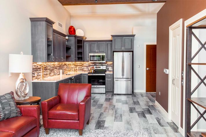 A modern kitchen with sleek cabinetry and red armchairs, featuring stainless steel appliances.