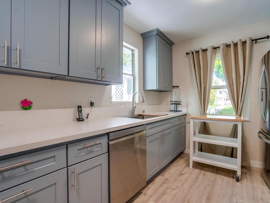 A modern kitchen with gray cabinets, a stainless steel dishwasher, and ample natural light.