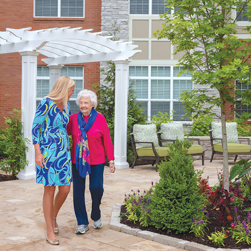 A caregiver accompanying an elderly woman in a beautifully landscaped outdoor space.