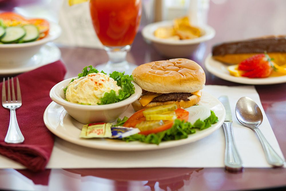 A meal consisting of a burger with a side of mashed potatoes and fresh salad on a dining table.