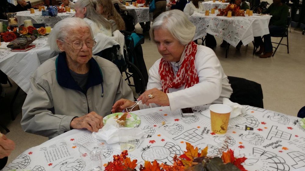 A person assisting an elderly individual during a community meal event.