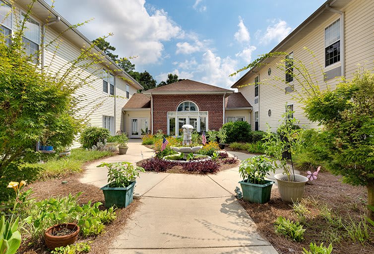 A landscaped courtyard with a central fountain and surrounding greenery leading to a building entrance.