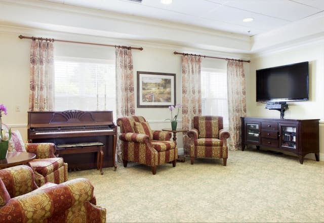 A cozy living room with a piano, comfortable chairs, and a television.